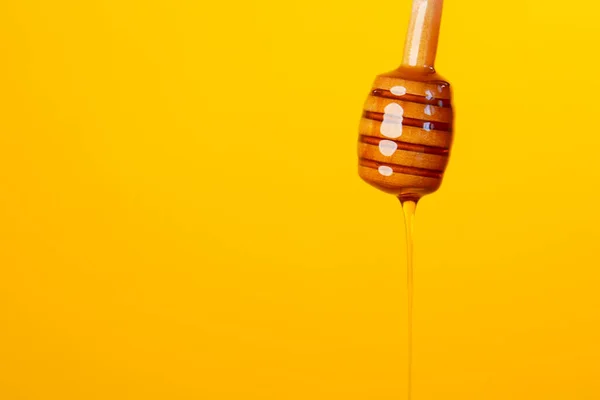 Krople miodu z łyżki miodu na żółtym tle — Zdjęcie stockowe