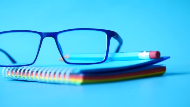 Blå färg anteckningsblock, glasögon och en penna på träbord — Stockvideo