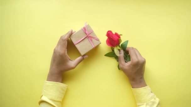 Ovanifrån av hand innehav presentförpackning och ros blomma på färg bakgrund — Stockvideo