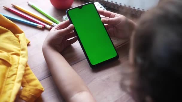 Zadní pohled na dítě dívka drží chytrý telefon bílý posazený na stole — Stock video