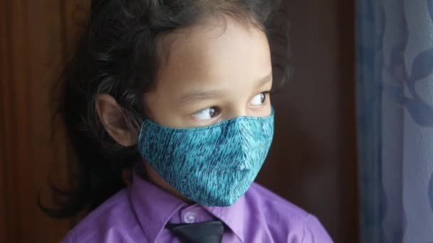 Грустный ребенок девочка в школьном платье в маске туза глядя в окно — стоковое видео