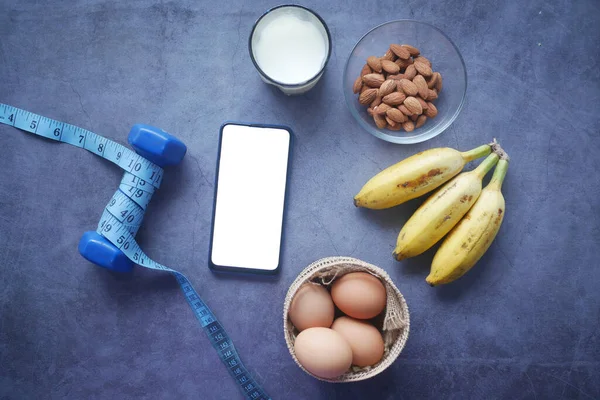Chytrý telefon s prázdnou obrazovkou, vejci, mlékem a mandlovou oříškou na stole — Stock fotografie
