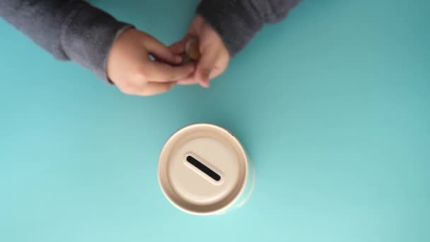 Kind hand besparen munten in een container op lichtgroene achtergrond bovenaanzicht — Stockvideo