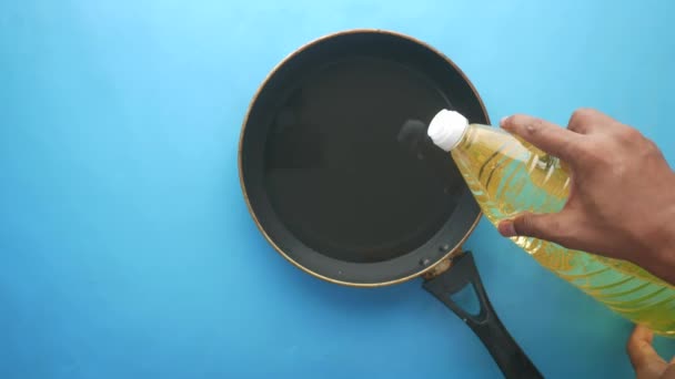 Pouring sunflower oil on cooking pan on blue background — Stockvideo