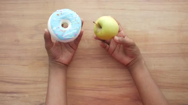 Ręka trzymając pączki i jabłko na stole — Wideo stockowe