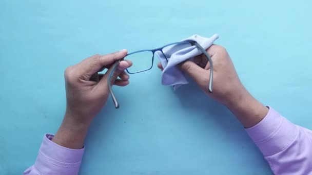 Cleaning eyeglass with tissue on blue background top view — Stock Video