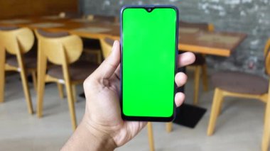  kafenin arka planında yeşil ekranlı akıllı telefon tutuluyor 