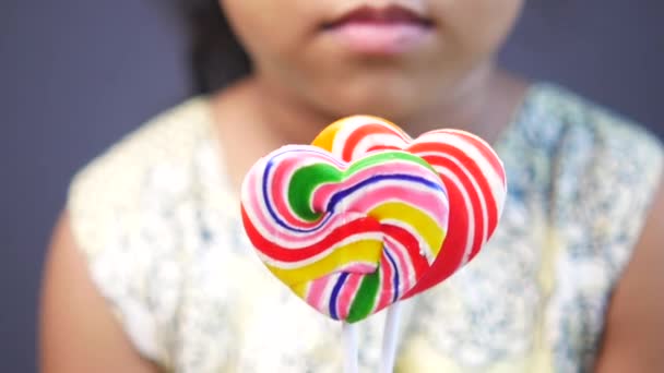 Child girl holding rainbow heart shape lollipop — Stockvideo