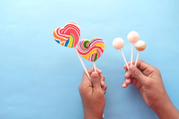 Holding rainbow heart shape lollipop on blue background — Stockfoto