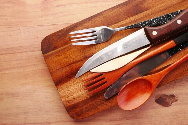 Tábua de corte de madeira, faca, colher e garfo na mesa — Fotografia de Stock