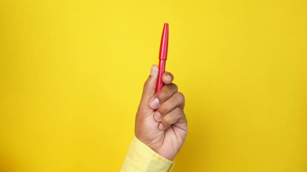 Hand hält einen roten Stift vor gelbem Hintergrund — Stockvideo