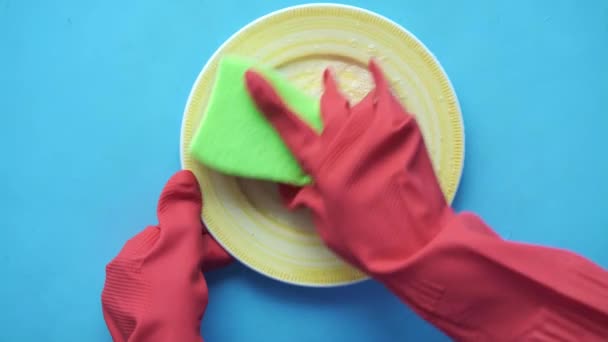 Губка, гумові рукавички та барвиста тарілка на синьому — стокове відео