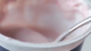 Plastik kabın içinde taze yoğurt ve masada kaşık. 