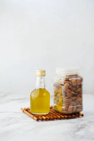 Minyak almond dalam botol dan kacang pada latar belakang putih. — Stok Foto