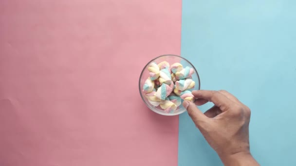Рука вибрати зефір цукерки в мисці на синьому — стокове відео