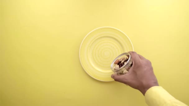 Vista superior de verter tuerca mixta sobre un plato sobre fondo amarillo — Vídeo de stock