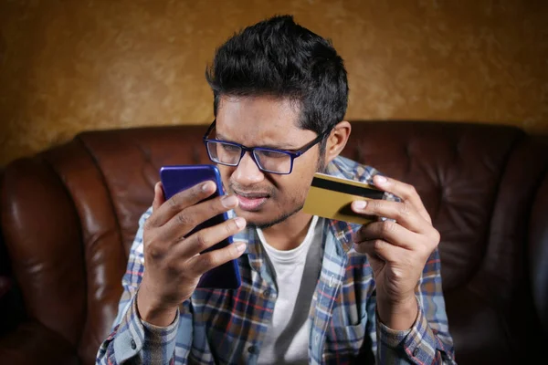 Boos man met credit card en smartphone terwijl ze op de bank — Stockfoto