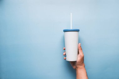  holding reusable eco coffee cup on blue with copy space.