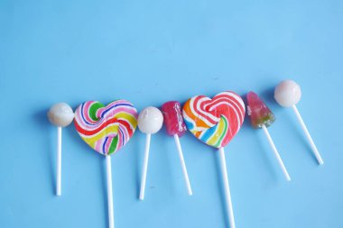 mavi arkaplanda gökkuşağı kalp şekilli lolipop 