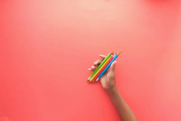 Menina segurando muitos lápis de cor no fundo vermelho — Fotografia de Stock