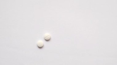 Yavaş çekimde beyaz renkli tıbbi haplar masaya düşüyor. 