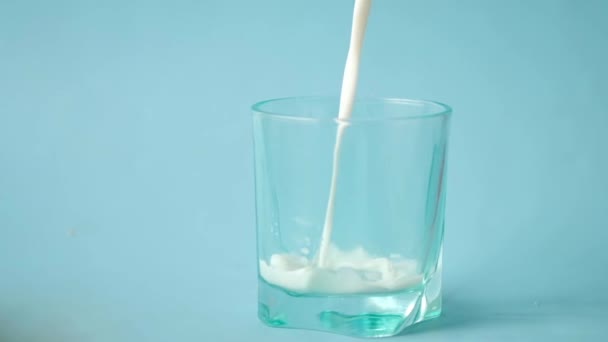 Mavi arka plandaki bardağa süt dökmenin yavaş çekimi — Stok video