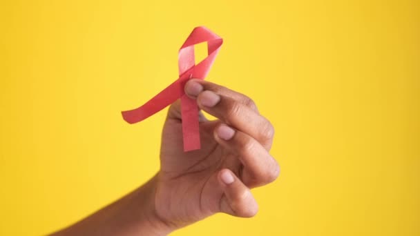 Hand holding red HIV ribbon against yellow — Stock Video