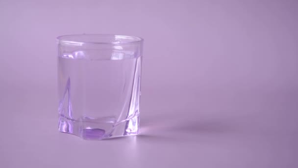Рука взять стакан воды на фиолетовом фоне — стоковое видео