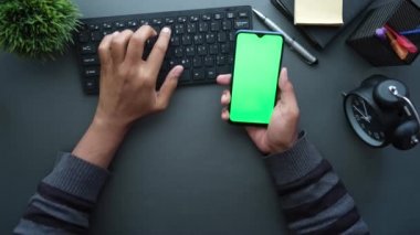 Ofis masasında boş ekranı olan akıllı telefonu tutan adamın üst görüntüsü 