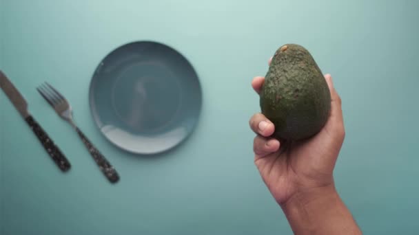 Het houden van een plak avocado tegen licht groene achtergrond — Stockvideo