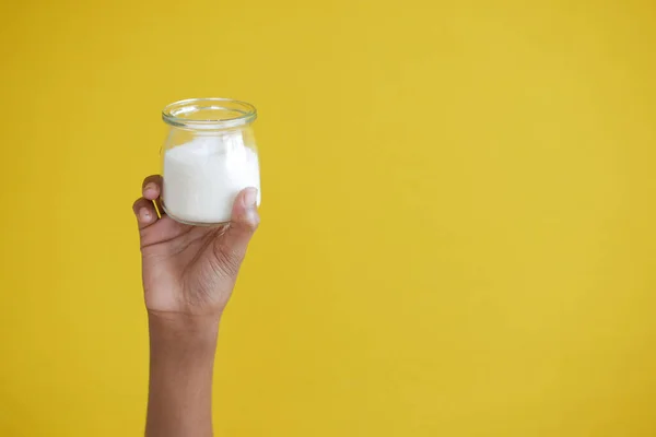 Trzymając słoik cukru białego na żółtym tle — Zdjęcie stockowe