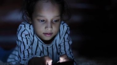 Çocuk kız gece akıllı telefon kullanarak yerde yatıyor. 