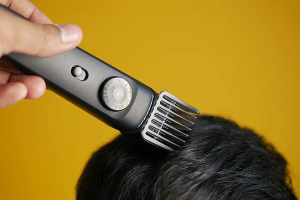 Corte de cabelo com um cortador de cabelo no fundo amarelo — Fotografia de Stock