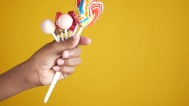 Hand holding lollipop candy on yellow background — Stock Video