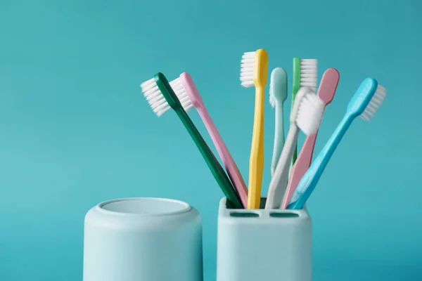 Cepillos de dientes coloridos en taza blanca contra fondo verde claro — Foto de Stock