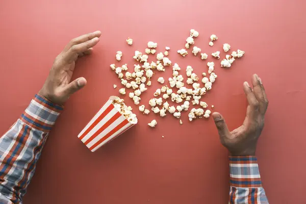 Hand greift nach Popcorn auf rotem Hintergrund — Stockfoto