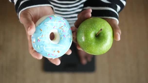 手にドーナツとりんごを持って体重計で . — ストック動画
