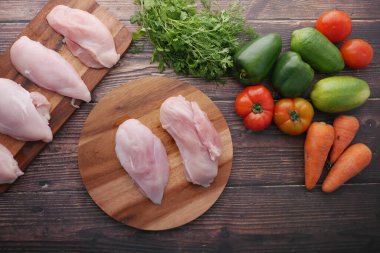 Sebzeli doğranmış bir tahtanın üstünde çiğ tavuk göğsü. 