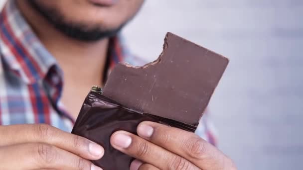 Молодой человек ест темный шоколад вблизи — стоковое видео