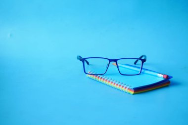 Not defteri, gözlük ve mavi arkaplan üzerine bir kalem. 