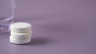 Fışkırtıcı çözünür tablet haplar ve mor arka planda bir bardak su. 