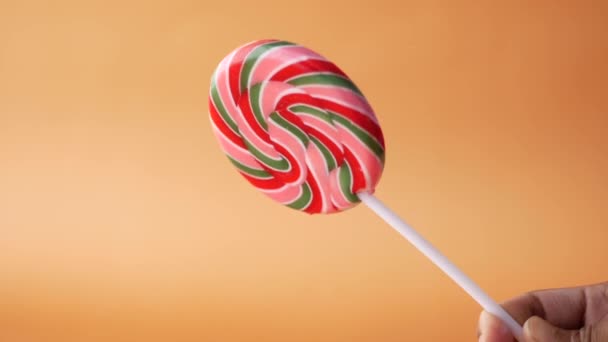 Close-up van het houden lolly candy tegen oranje achtergrond — Stockvideo