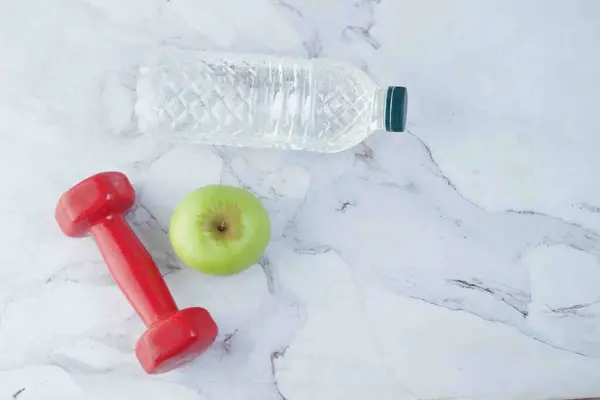 Agua potable fresca, manzana y una mancuerna de color rojo en la mesa — Foto de Stock