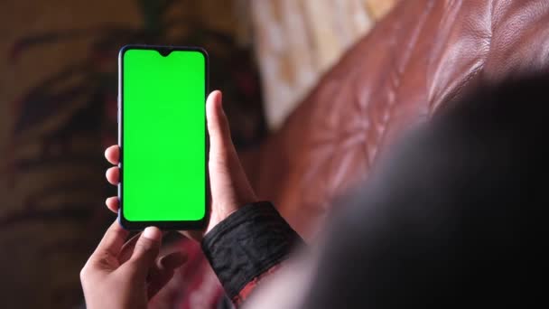 Hombres jóvenes sosteniendo el teléfono inteligente con pantalla verde acostado en el sofá — Vídeos de Stock