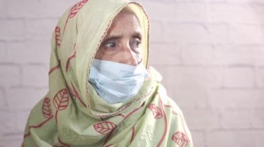 Cerrahi maske takan yaşlı bir Hintli kadının portresi.