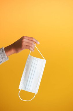  Adam, sarı arka planda cerrahi yüz maskesi tutuyor. 