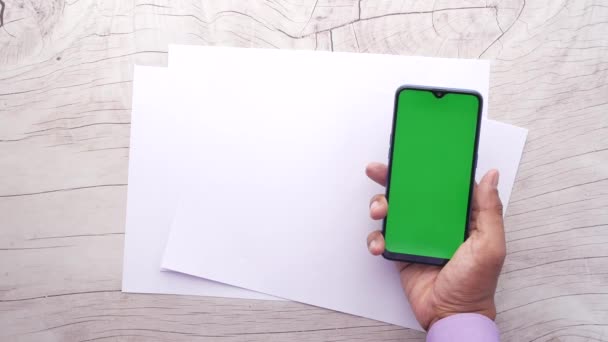 Bovenaanzicht van de hand van de mens met behulp van smartphone en leeg papier op tafel — Stockvideo