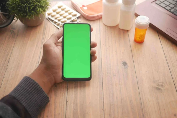 Hand hält Smartphone und Medikamententabletten auf Schreibtisch — Stockfoto