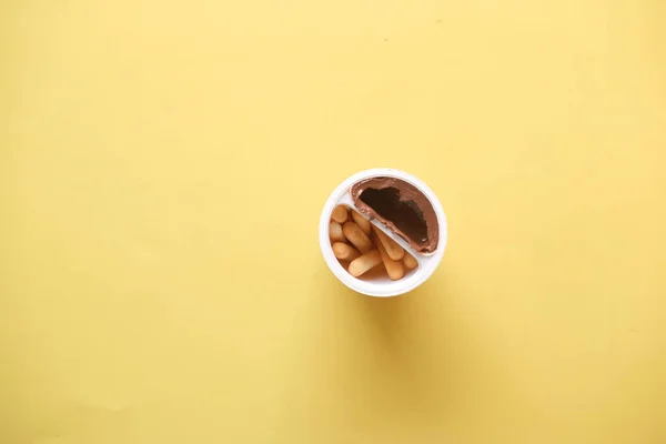 Pałeczka chlebowa z kremem do smarowania czekolady w pojemniku na żółtym tle — Zdjęcie stockowe