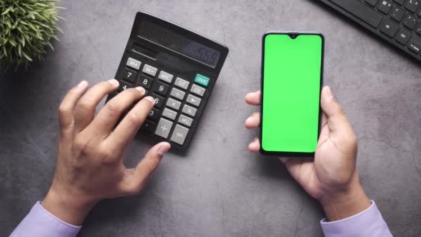 Vista dall'alto della mano dell'uomo utilizzando la calcolatrice e tenendo in mano uno smartphone — Video Stock